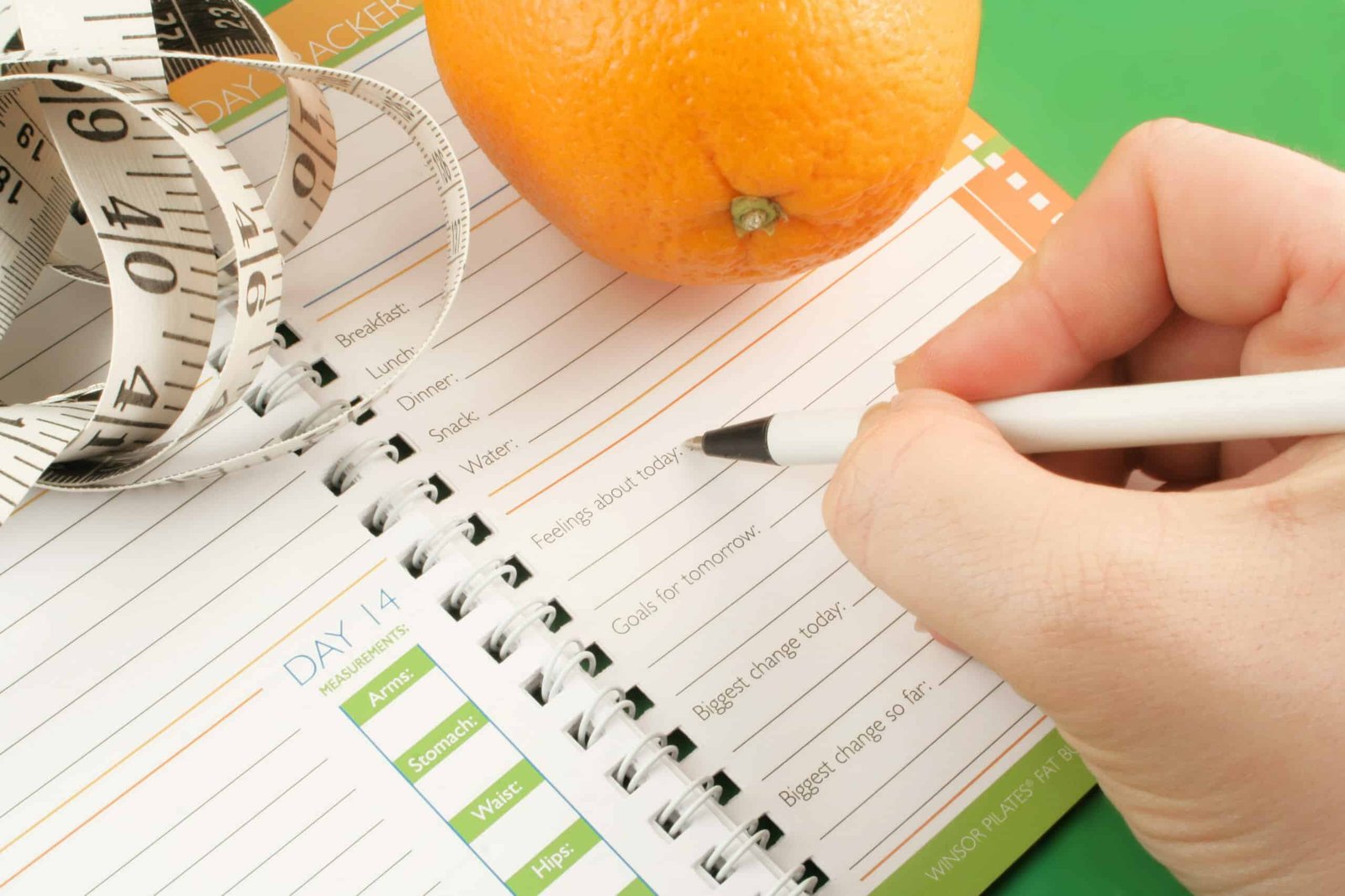 writing in a diet and nutrition journal with orange and tape measure to the side